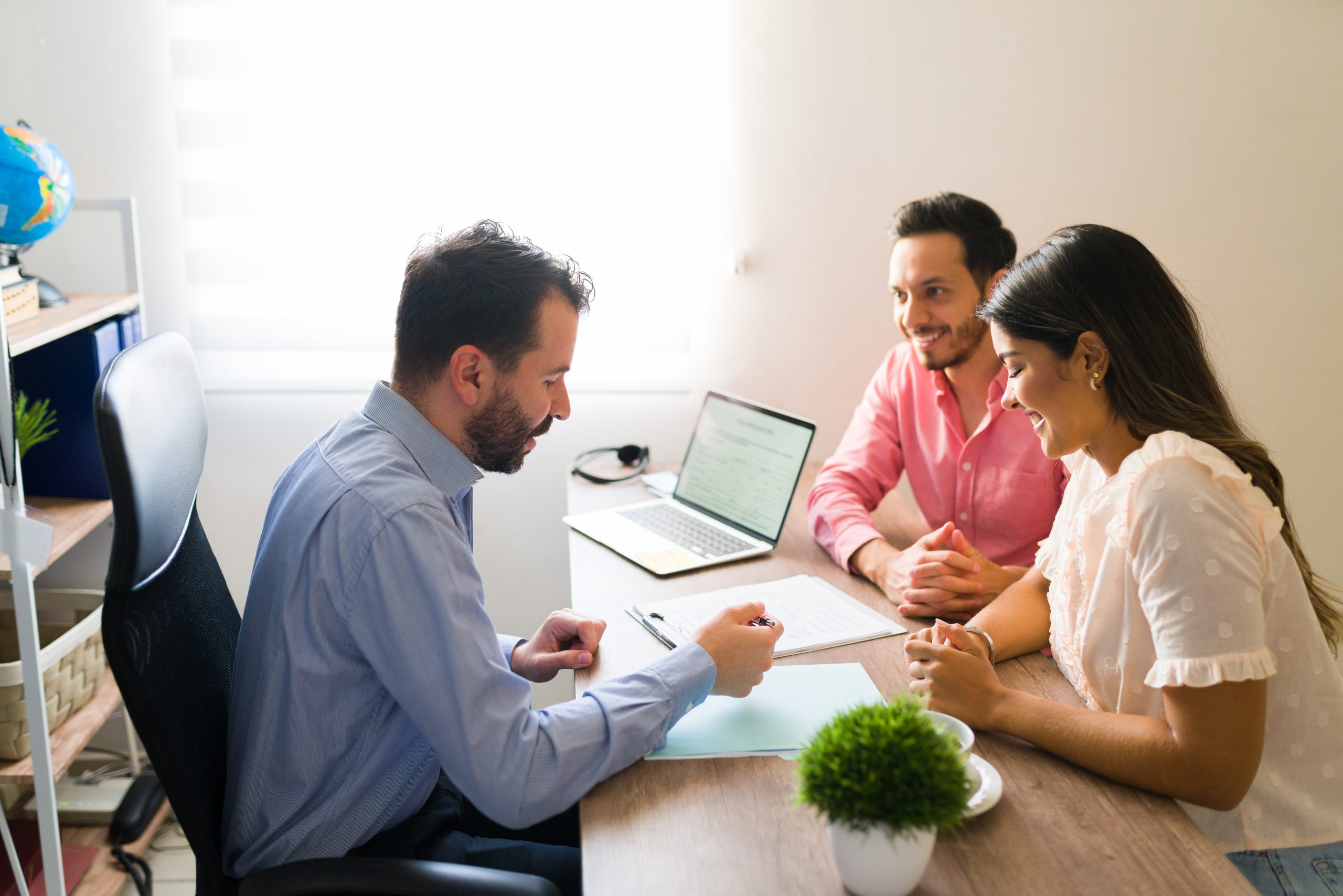 Three people, two clients and an insurance agent, review documents on a desk with a laptop